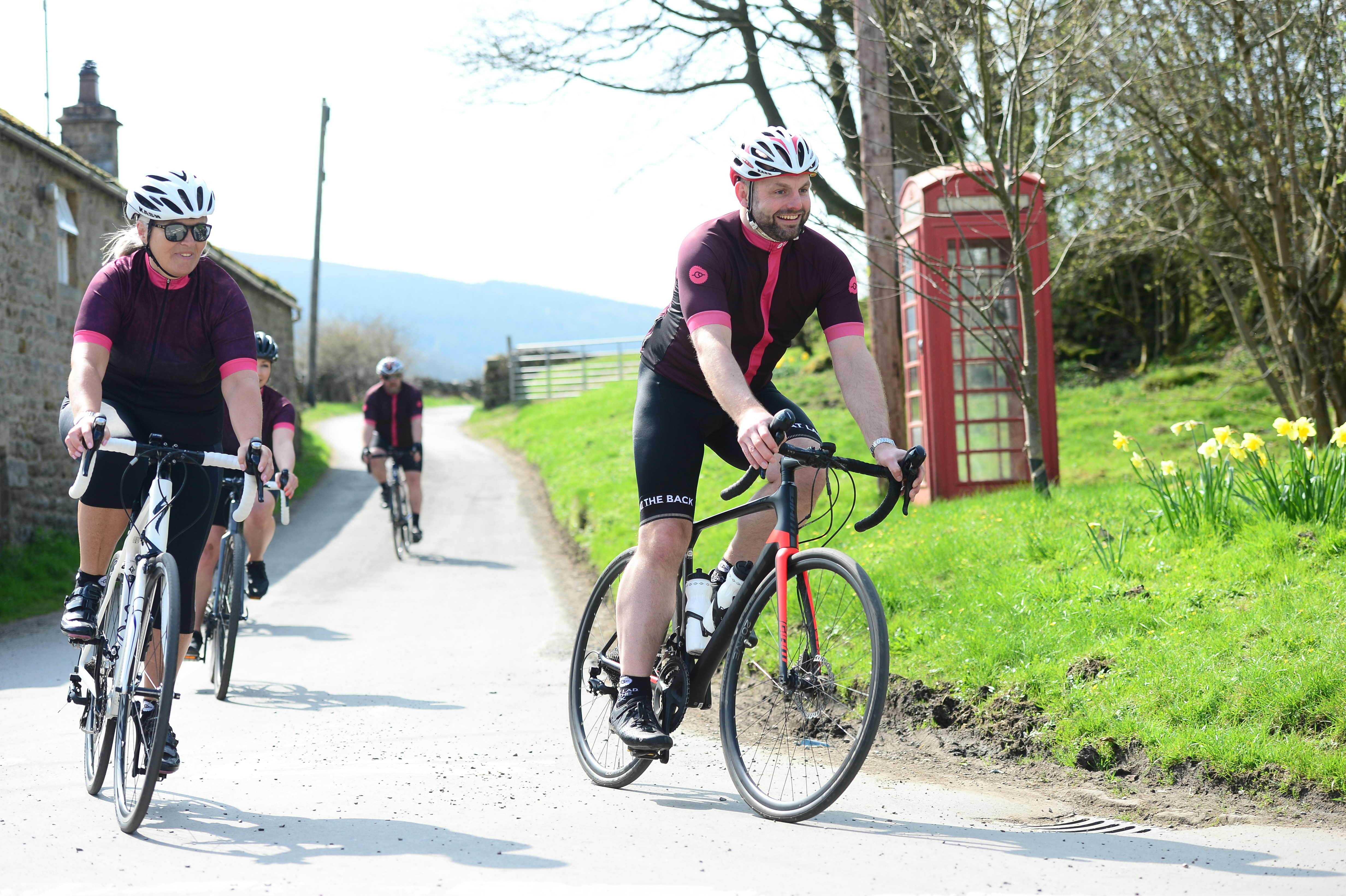 cyclists riding along a country lane in rural Yorkshire village with traditional red phone box